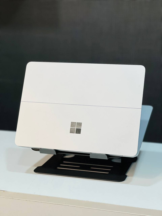 نمای پشتی لپتاپ با بدنه فلزی و مقاوم، نشاندهنده استحکام و طراحی مینیمالیستی است. لوگوی مایکروسافت بر روی بدنه قرار دارد که به زیبایی دستگاه افزوده است.